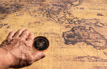 Classic round compass in hand on background of old vintage map of world as symbol of tourism with compass, travel with compass and outdoor activities with compas