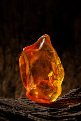 Beauty of natural raw amber. A piece of yellow opaque natural amber on large piece of dark stoned wood.