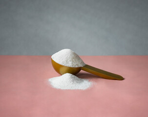 Gold measuring spoon with collagen on pastel pink gray background. Powdered hydrolyzed fish collagen supplement.