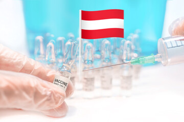 Hands holding a vaccine vial and a syringe with rows of the same capsules and a flag of Austria in the background, illustrating plans for global vaccination against Covid-19 (SARS-CoV-2, coronavirus).