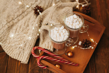 Top view of hot winter drink chocolate or cocao with marshmallows and sweet cane on wooden background lights garlands. Cozy winter merry christmas and new year concept