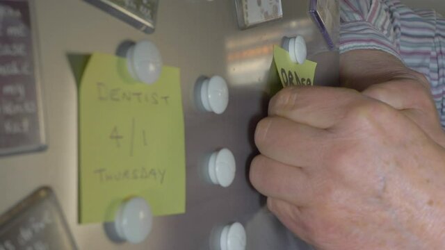 Closeup of a man&rsquo;s hands sticking a note to Order Food on a fridge door, using magnets.