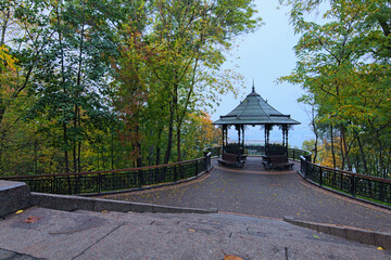 Astonishing landscape of panoramic viewing platform with beautiful arbor in autumn tree leaves border. Foggy morning in the Saint Volodymyr Hill. Blurred view of Dnipro River and the surrounding