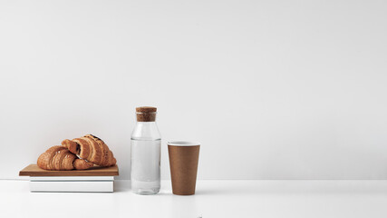 Croissants on a wooden board, a bottle with a cork stopper and a paper disposable glass on a white background. Natural and eco-friendly materials. Copy space, mock up