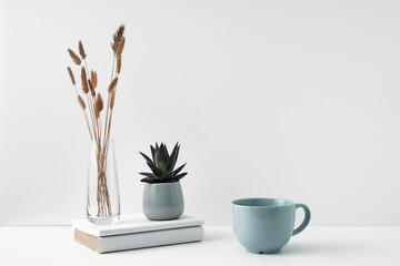 A mug and potted houseplant, a stack of books and a transparent vase. Eco-friendly materials in interior decor, minimalism. Copy space, mock up.