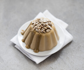 Vegan Panna cotta cream sunflower paste with seeds and sauce on a plate on a linen napkin on a light gray background top view