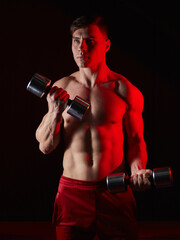 Naklejka na ściany i meble man bodybuilder lifting dumbbells working focused on his biceps in front of the mirror at the gym. Athlete holding two dumbbells showing straining veins on hands bubble guts.