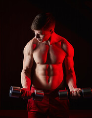 man bodybuilder lifting dumbbells working focused on his biceps in front of the mirror at the gym....
