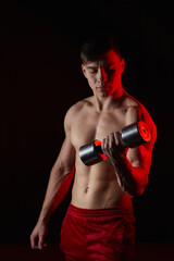 Fototapeta na wymiar Sporty young man training with dumbbells against dark background