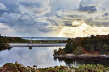 Obraz premium Image of Val de la Mare Reservoir with St Ouens bay in the background with stormey clouds at sunset.