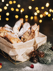 Italian biscotti cookies, lying in a basket, next to a New Year's spruce branch. Scattered with almonds and cranberries. Christmas cookies with nuts. Powdered sugar. Christmas mood. New Year's food.