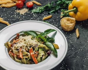 Vegetable pasta sprinkled with parmesan and garnished with basel. Nearby are sprinkled pasta, bell peppers, zucchini and tomatoes, greens. Menu for cafes and restaurants. Ingredients for the pasta.
