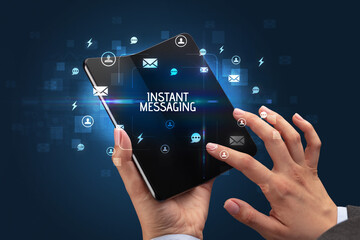 Businessman holding a foldable smartphone with INSTANT MESSAGING inscription, social networking concept