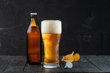 Beer bottle and bottle caps. A bottle of dark beer and a glass with foam. Beer with chips.