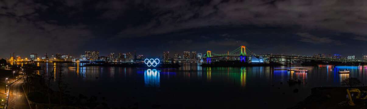 Tokyo, Japan - January 24, 2020: A panorama picture of the Tokyo Bay, featuring the illuminated Rainbow Bridge, and the lit Olympic Rings, at night.