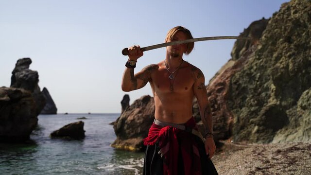 Mature Tattoed Man Holding Swords Ready To Fight on the rocky sea background - Portrait Of A Handsome Muscular Ancient Warrior With A Swords. Martial art concept