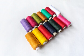 Multicolor sewing thread spools laying diagonally on isolated white background.