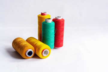 Five different yellow, red and sea green colored sewing thread spools on isolated white background.