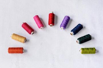 Multicolor sewing thread spools laying in semicircle shape on isolated white background.