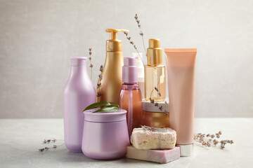 Set of hair cosmetic products and flowers on grey table