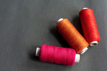 Red, pink and orange colored sewing thread spools on isolated black background.
