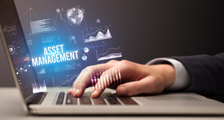 Businessman working on laptop with ASSET MANAGEMENT inscription, new business concept