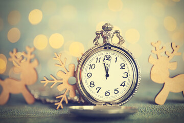 Pocket watch and festive decor on table against blurred lights. New Year countdown