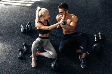 Gordijnen young man and woman sitting on the floor and giving each other five in the gym, fitness people after workout in the gym © Shopping King Louie
