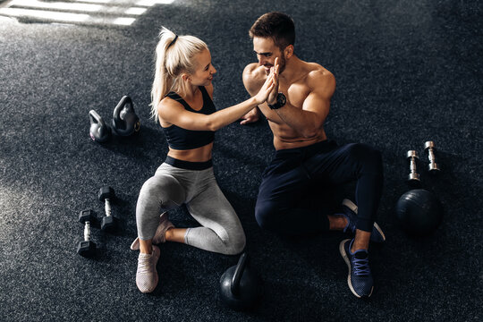 young man and woman sitting on the floor and giving each other five in the gym, fitness people after workout in the gym