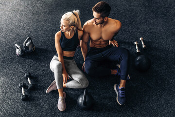 Fototapeta na wymiar Young couple of athletic people sitting together on the floor of the gym, with dumbbells, together after training in the gym