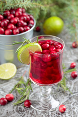 Glass of cranberry drink with berries, lime, and rosemary.