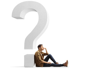 Sad and pensive young man sitting on the floor and leaning on a question mark
