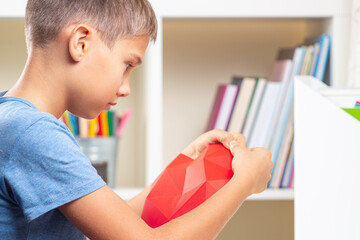 Boy looking video tutorial and making red polygonal paper heart. Education, learning, paper craft, entertainment at home