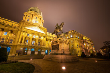 The illuminated main facade of the historic Royal Palace - Buda Castle in Budapest with the statue of Savoyai Eugen - Hungary at night