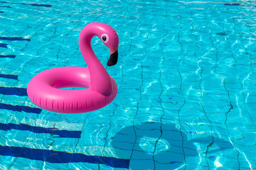 Summer time. Pink inflatable flamingo in pool water for summer beach background. Funny bird toy for...