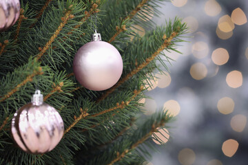 Fototapeta na wymiar Shiny lilac balls hanging on Christmas tree against festive lights