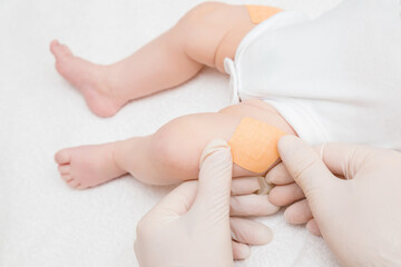 Fototapeta na wymiar Doctor hands in white rubber protective gloves putting adhesive bandage on infant leg after injection of vaccine. Medical concept. Closeup.