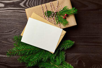 Christmas greeting card mockup with gift box and fir tree branches on wooden table