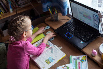 Little girl in eyelgasses studying online and using her laptop at home