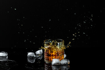 The glass of cognac or brandy isolated on a black background. alcohol cocktail. ice cubes fall into...