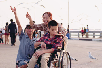 Asian Disabled child on wheelchair and parents the outdoors ​nature​ and seagull birds background​,Boy frightened expression afraid of the bird, Happy disability kid travel in family holiday concept.
