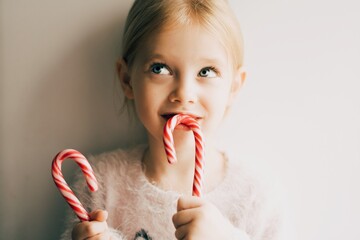 Little smiling girl eating new years candies, red Christmas candy. Close up portrait of a little child. New year concept. 2021. - 398767401