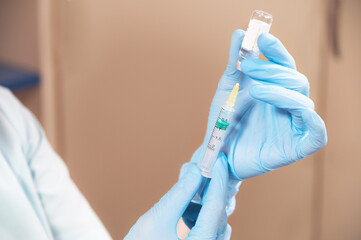 Close-up of a beautician's hand in rubber gloves is filling a syringe with liquid for cosmetic...