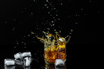 Isolated shot of whiskey with splash on dark background, brandy in a glass splashes from falling ice fly in different directions. freeze motion