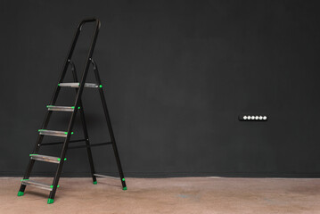 Black step ladder on the black color wall background.