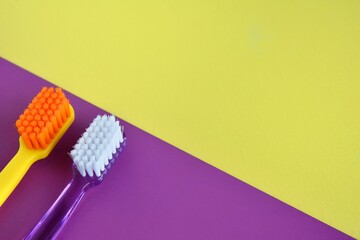 two plastic purple and yellow toothbrushes on color block paper background. Health care concept. Man and woman teeth hygiene. Living together. 