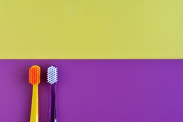 two plastic purple and yellow toothbrushes on color block paper background. Health care concept. Man and woman teeth hygiene. Living together. 