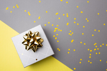 Gift box with yellow ribbon and confetti on ultimate gray paper background. Colors of the 2021 year. Top view