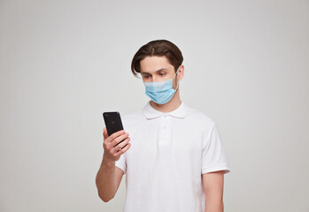 Fototapeta na wymiar European man in a mask uses a telephone. Conceptual photo on the theme of the covid-2019 pandemic.