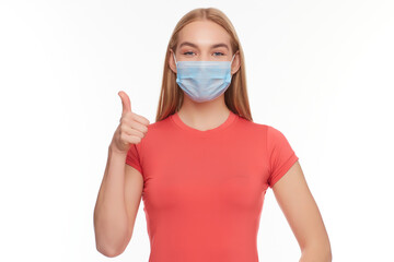 European girl in a medical mask, shows thumb up. Conceptual photo on the theme of the Covid 2019 pandemic.